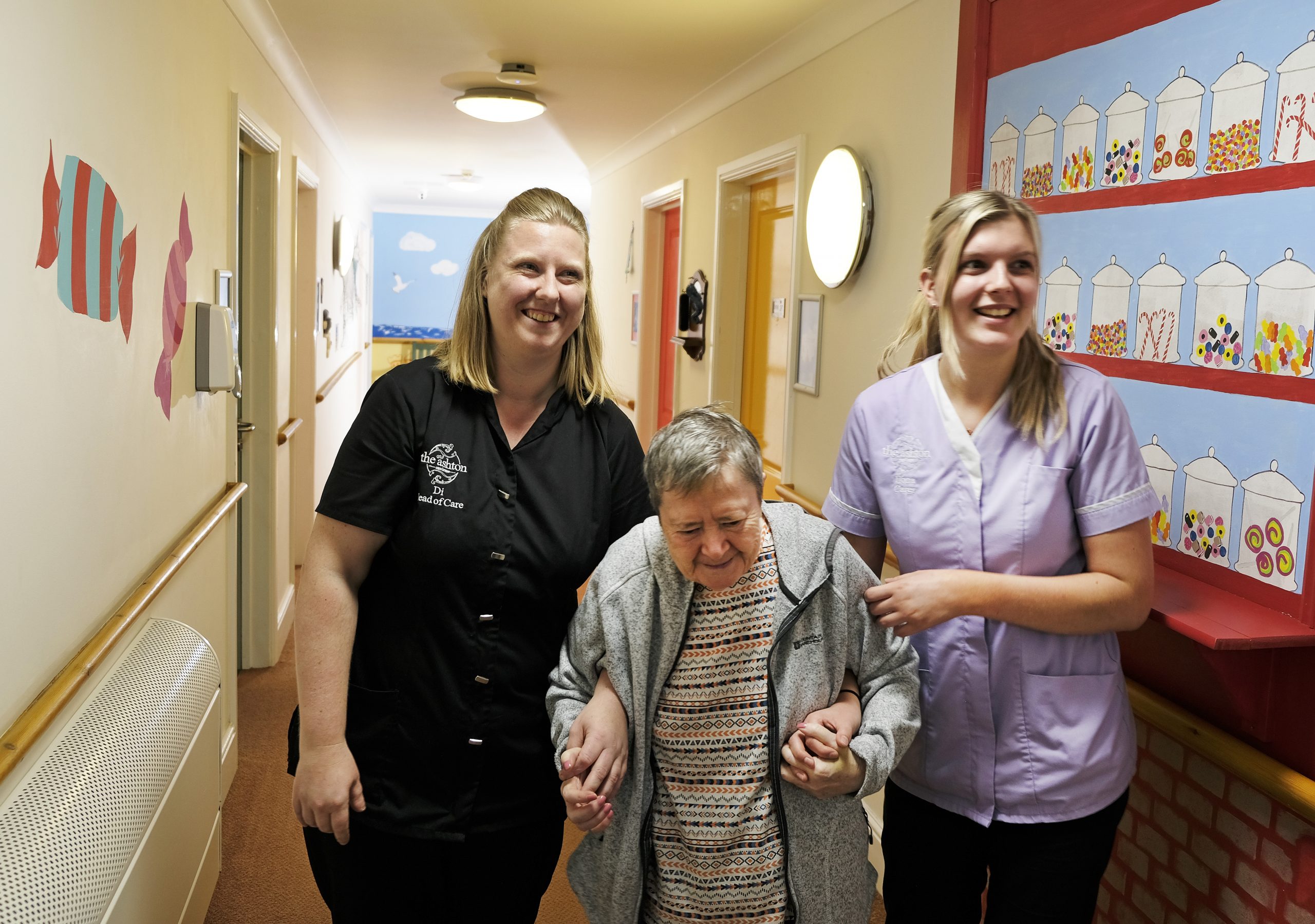A female residents holding hands with two female care assistants. One wearing black and the other wearing purple.