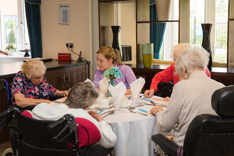 Four female residents playing bingo with a female carer wearing purple.