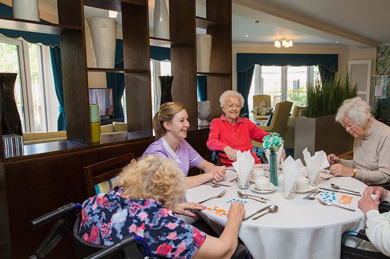 Three female residents playing bingo with a female carer wearing purple. All laughing and smiling.