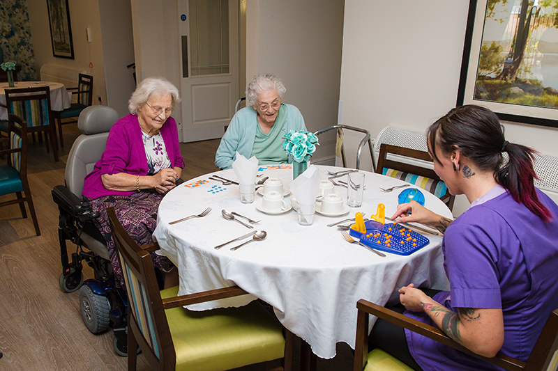 Dressed table with two female residents playing bingo with a female carer in purple.