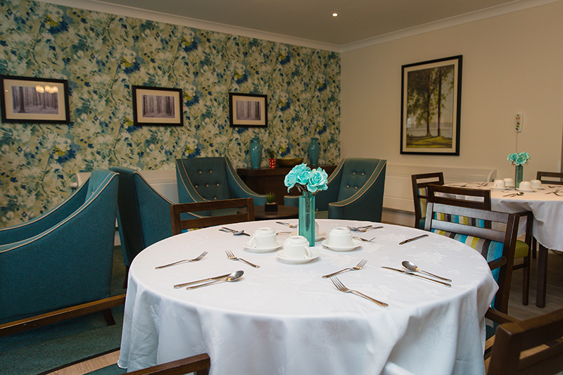 Dressed dining room table with seating area in the background and floral blue wallpaper.
