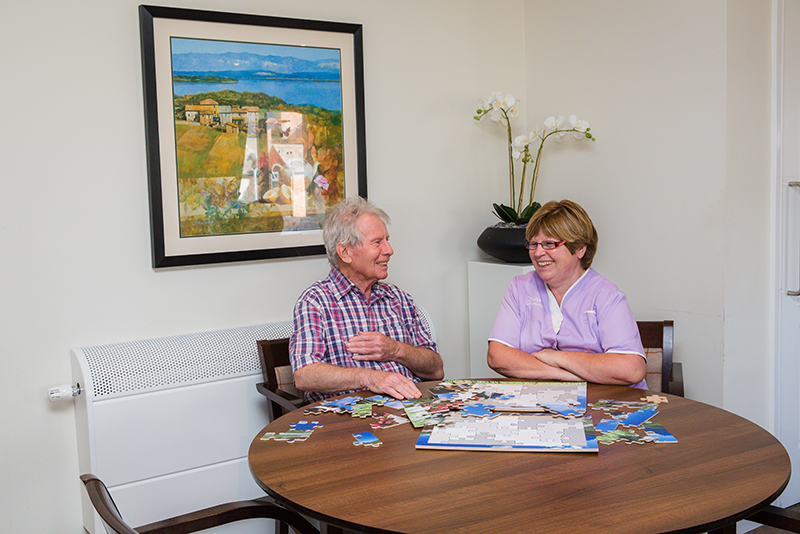 A male resident and female nurse laughing while playing a puzzle.