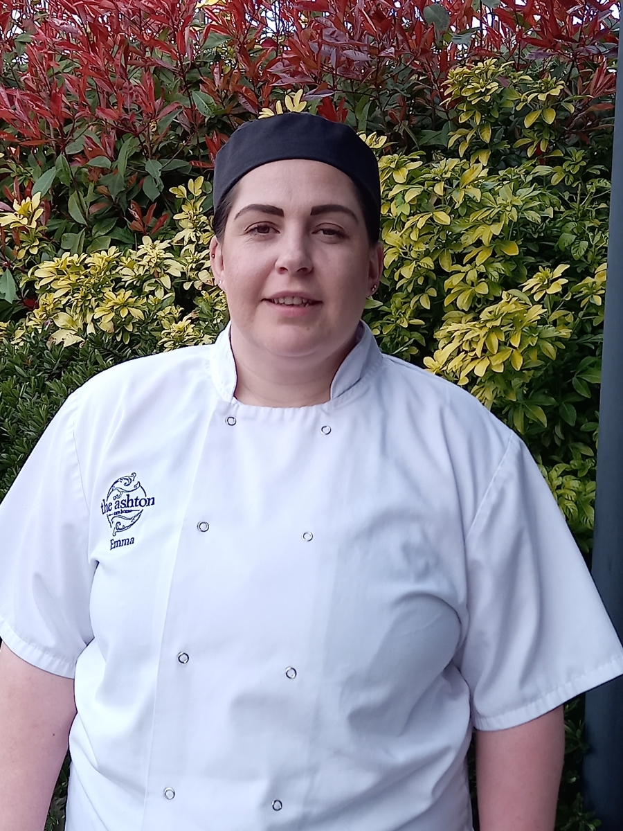 Female chef wearing a white uniform and black hat.