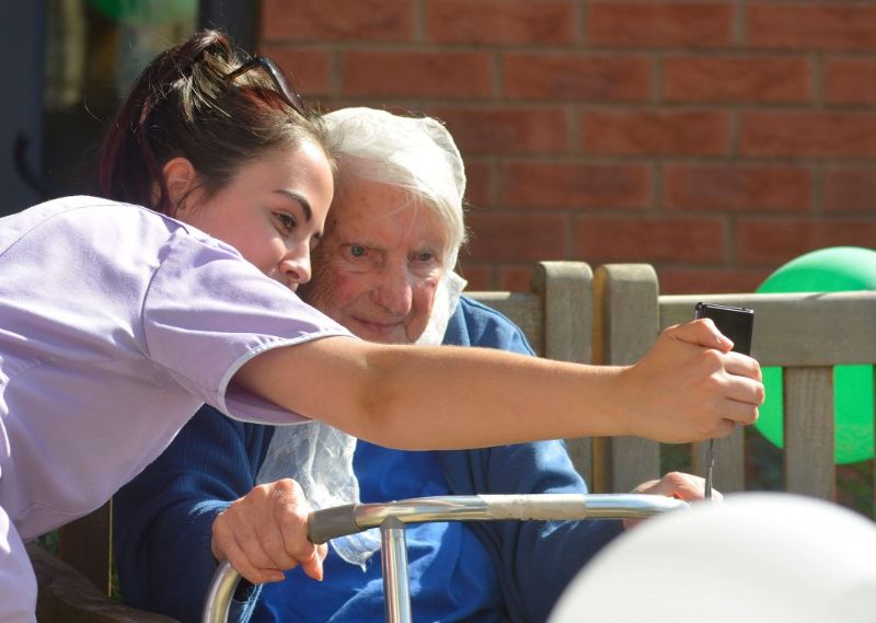 A male resident smiling having a selfie with a female carer in a purple uniform and black hair.