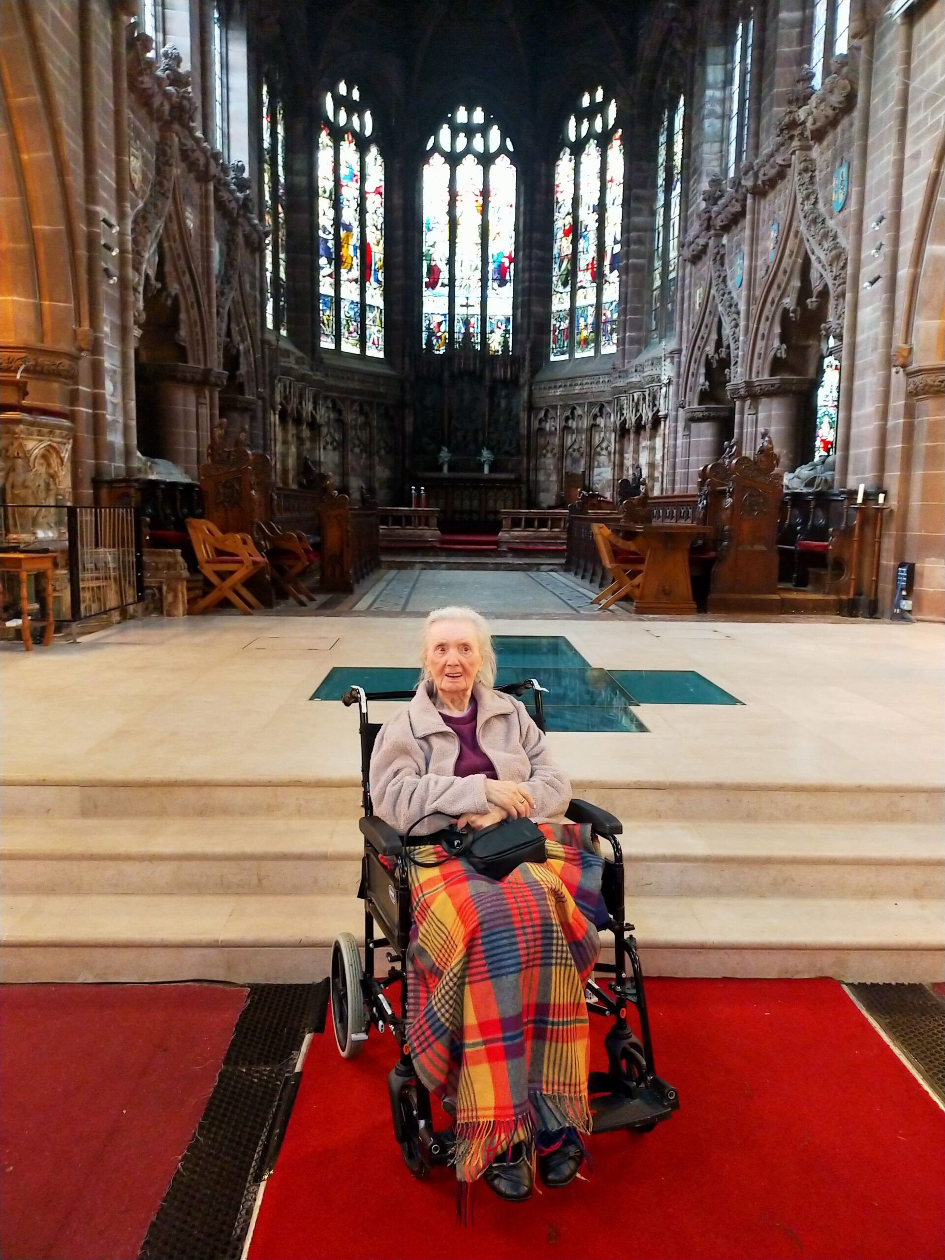 A female resident in a wheelchair, covered in a bright patterned blanket in a Cathedral.