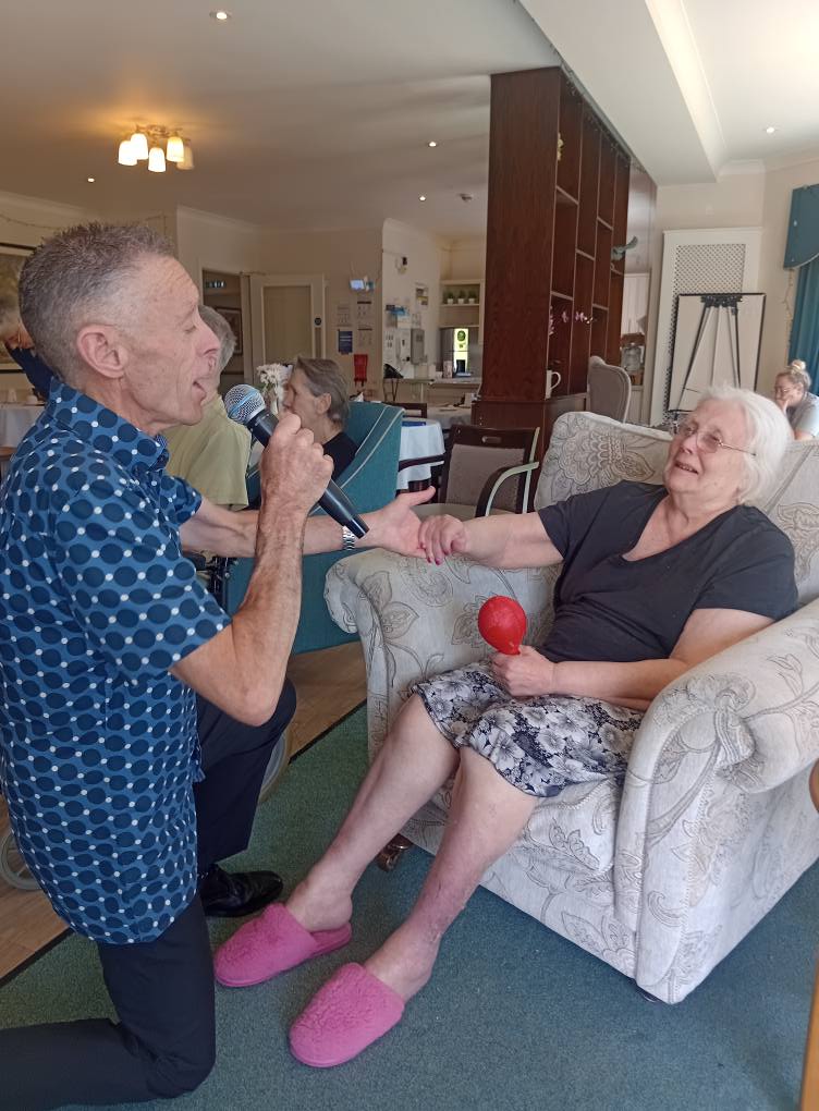 man singing to an older lady sat down in a chair