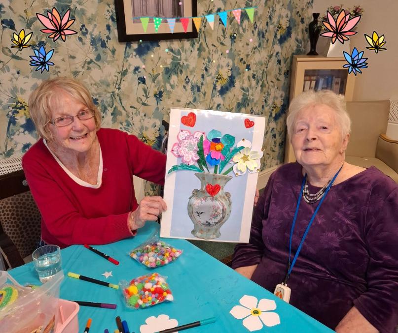 two older ladies holding up a picture of flowers