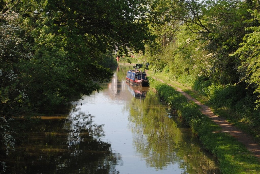 Green landscape with a river flowing through, featuring a barge floating on the water.