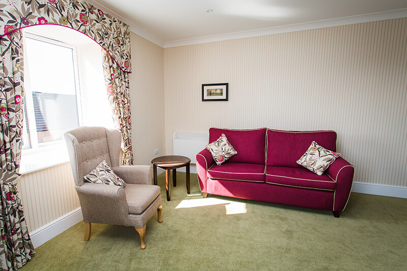 A lounge room featuring a burgundy red sofa and a gray armchair.