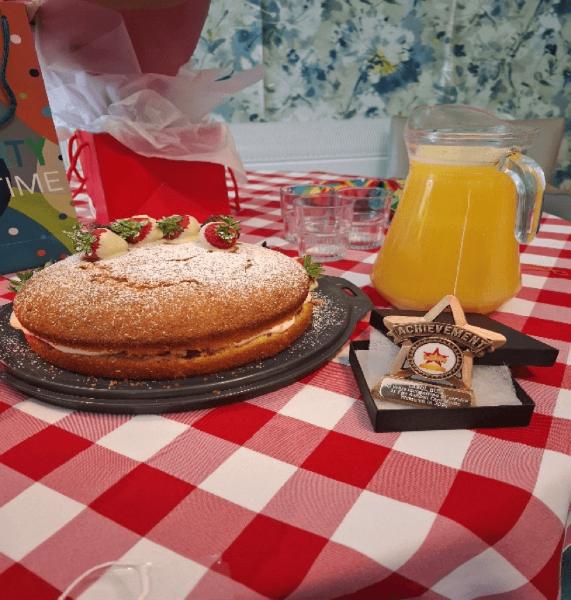 A Victoria sponge cake and a jug of orange juice on a table.