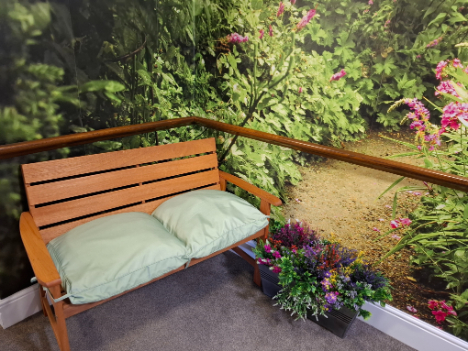 a wooden bench with green cushions on and a pot of flowers