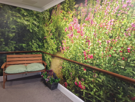 a wooden bench with green cushions on and a pot of flowers