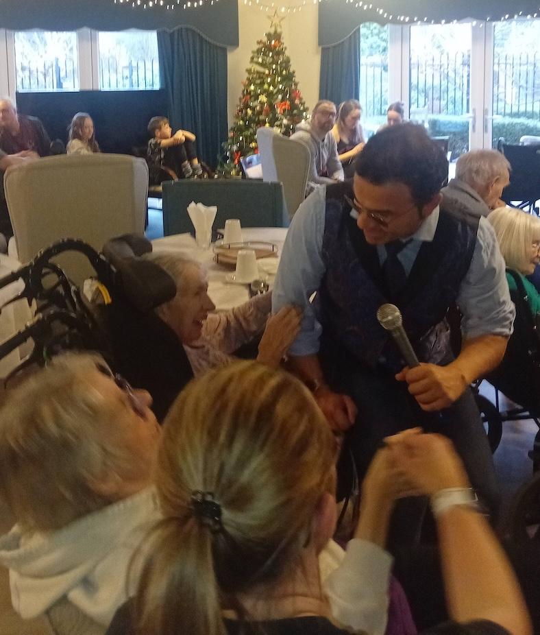 male singer sat with older adults in a care home performing for them
