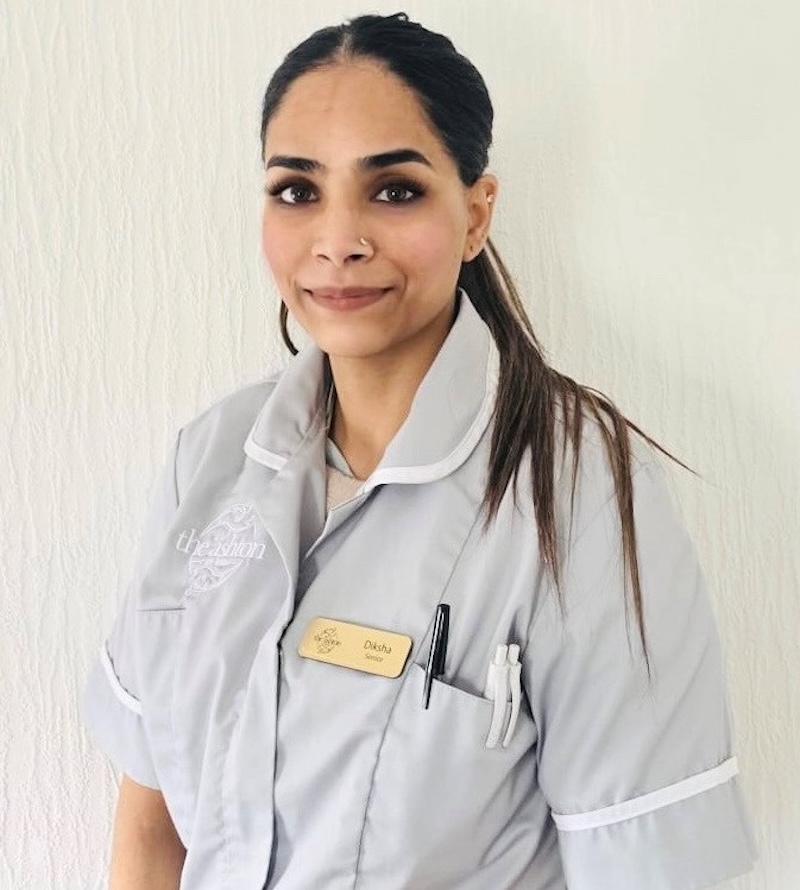 woman with brown hair wearing a blue senior care assistant uniform smiling having her photo taken for the team page