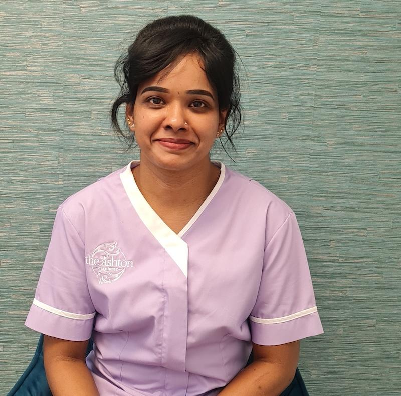 woman with brown hair wearing purple care assistant uniform smiling having her photo taken for the team page