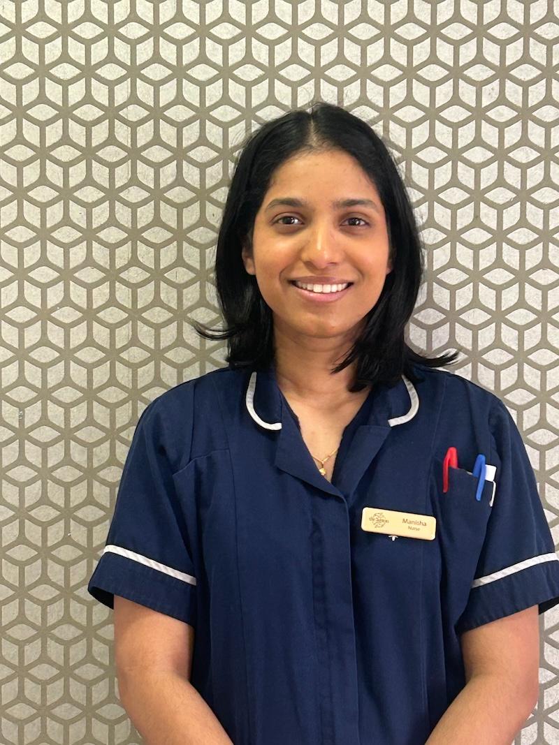 woman with brown hair wearing a navy blue nurse uniform smiling having her photo taken for the team page