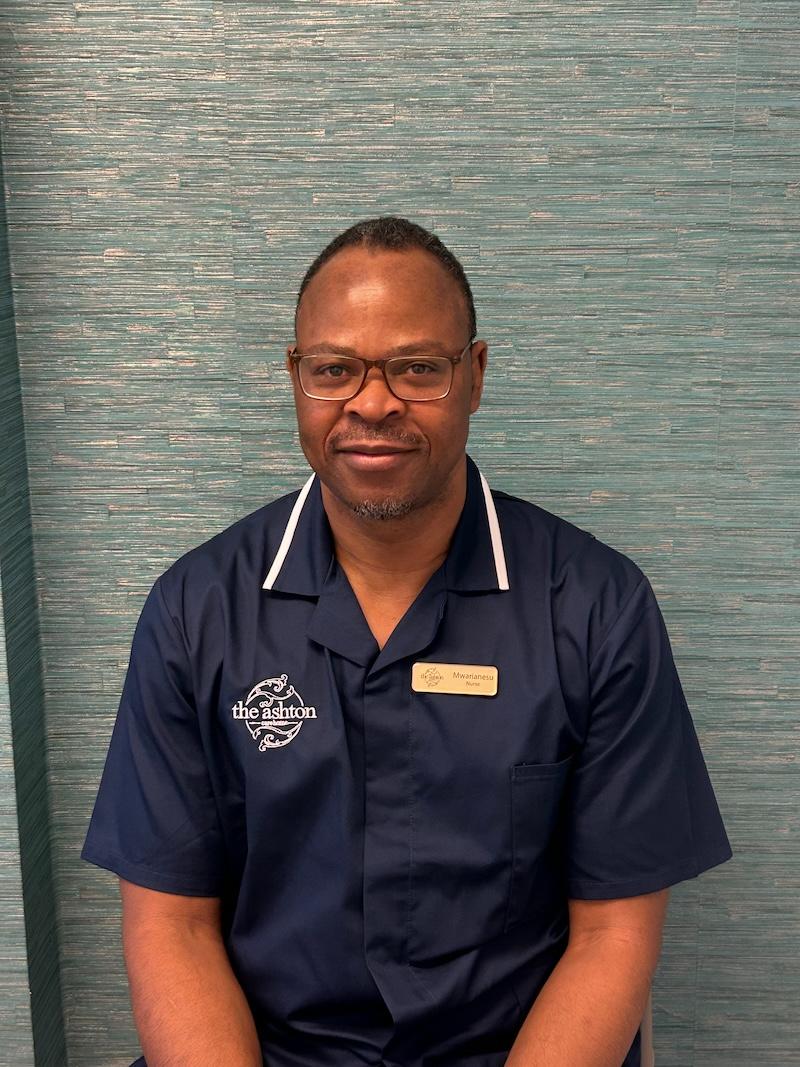 man with brown hair wearing a navy blue nurse uniform smiling having his photo taken for the team page