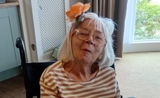 older lady in a wheelchair smiling wearing an orange headband