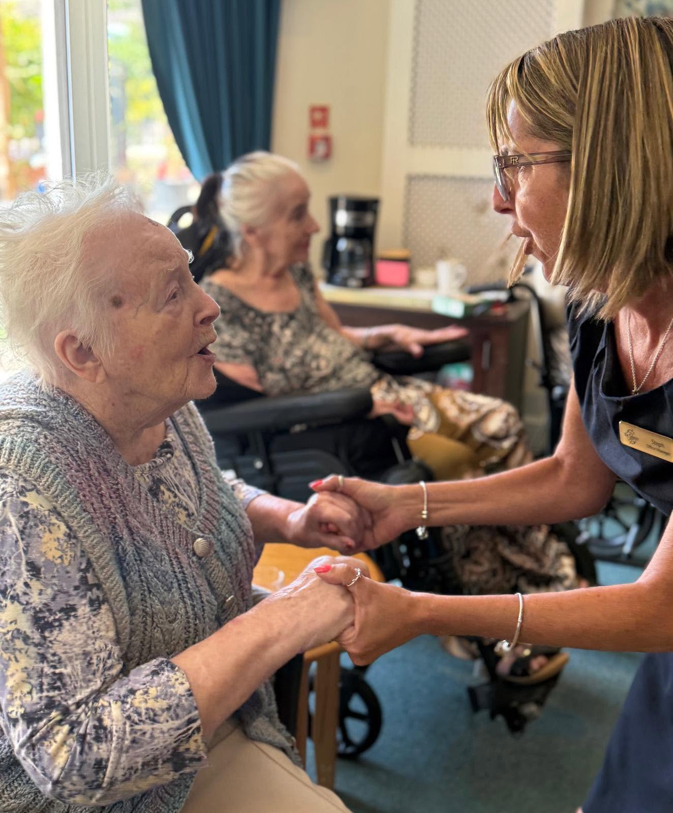 resident and carer smiling holding hands