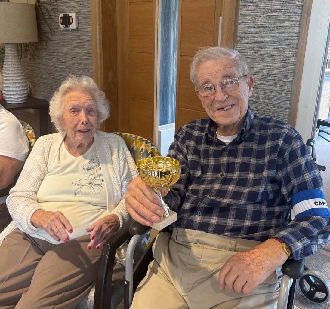 an older man and older lady sat down holding up a trophy